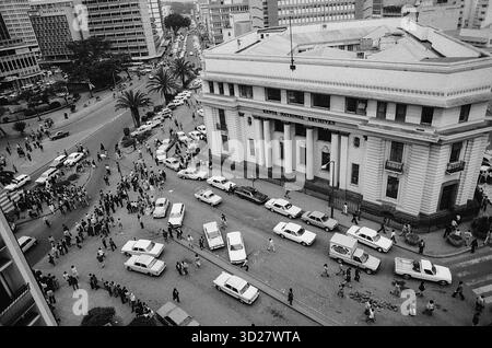 Die belebte Straßenszene von Nairobi fängt das Herz der kenianischen Hauptstadt ein. Das Foto wurde 1972 aufgenommen und zeigt einen dichten Verkehrsfluss entlang der Kenyatta Avenue, der von dem imposanten Gebäude der National Bank of Kenya dominiert wird. Fußgänger füllen die Bürgersteige und tragen so zur lebhaften Energie der Stadt bei. Dieses Bild bietet einen Einblick in die urbane Landschaft von Nairobi während eines entscheidenden Moments seiner Geschichte. Stockfoto
