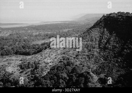 Panoramablick vom Lake Manyara Aussichtspunkt, Tansania. Dieses dramatische, monochrome Bild fängt die weitläufige Schönheit des Manyara-Nationalparks ein. Sanfte Hügel und dichte Vegetation erstrecken sich bis zum fernen See und bieten einen atemberaubenden Blick auf Tansanias vielfältige Landschaften. Stockfoto