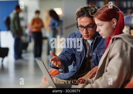 Junger asiatischer Mann, der der jungen kaukasischen Frau das Projekt mit Laptop erklärt Stockfoto
