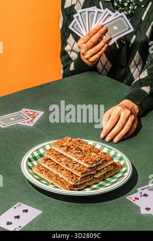: Pokerspiel-Thema Nut Brittle Stack auf karierter Platte mit Spielkarten und Hand auf grünem Tisch Stockfoto
