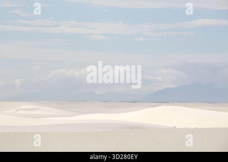 Eine riesige Weite weißer Sanddünen erstreckt sich unter einem ruhigen Himmel voller Wolken. Die sanften Kurven der Dünen schaffen eine friedliche und ruhige Atmosphäre Stockfoto