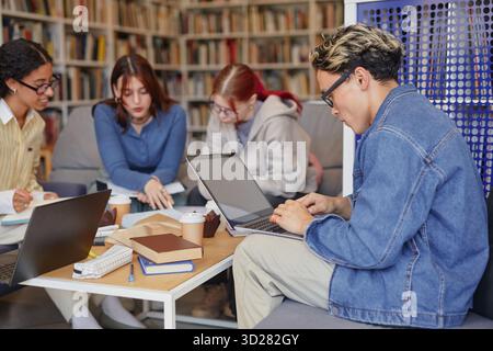 Verschiedene Gruppe junger Erwachsener, die an einem Projekt in Bibliotheksumgebung zusammenarbeiten Stockfoto