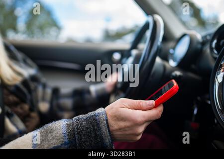 Autofahrerin, die mit dem Smartphone abgelenkt wird, während sie im Verkehr Auto fährt, SMS schreibt und Nachrichten liest Stockfoto