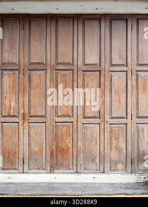 Nahaufnahme einer alten, verwitterten Holzfalttür. Die rustikalen braunen Paneele zeigen eine Vintage-Textur und bilden den Hintergrund eines traditionellen Hauses Stockfoto