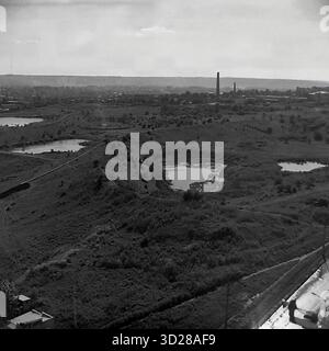 Archiv Schwarzweißfoto aufgenommen in Sloviansk, Ukraine, im August 1997. Dies ist ein Panoramablick über die Stadt aus einem hohen Winkel, der „vom SKTB“ (Special Design and Technological Bureau) übernommen wurde. Die Aufnahme erfasst eine riesige urbane Landschaft und zeigt die Wohnviertel der Stadt am Horizont, einschließlich mehrstöckiger Gebäude. Im Vordergrund ist eine große Grünzone, möglicherweise ein Park- oder Waldgürtel, zu sehen, an der eine Hauptstraße entlang verläuft. Dieses Bild dokumentiert das Erscheinungsbild der Stadt in den späten 1990er Jahren Stockfoto