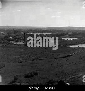Archiv Schwarzweißfoto aufgenommen in Sloviansk, Ukraine, im August 1997. Dies ist ein Panoramablick über die Stadt aus einem hohen Winkel, der „vom SKTB“ (Special Design and Technological Bureau) übernommen wurde. Die Aufnahme erfasst eine riesige urbane Landschaft und zeigt die Wohnviertel der Stadt am Horizont, einschließlich mehrstöckiger Gebäude. Im Vordergrund ist eine große Grünzone, möglicherweise ein Park- oder Waldgürtel, zu sehen, an der eine Hauptstraße entlang verläuft. Dieses Bild dokumentiert das Erscheinungsbild der Stadt in den späten 1990er Jahren Stockfoto