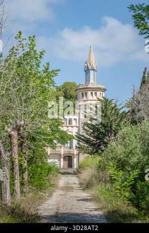 Vorderansicht der modernistischen Masia Cal Pla, ein Kulturgut von lokalem Interesse, mit seinem zentralen Turm, durch einen bewachsenen Pfad in Cunit, Spanien Stockfoto