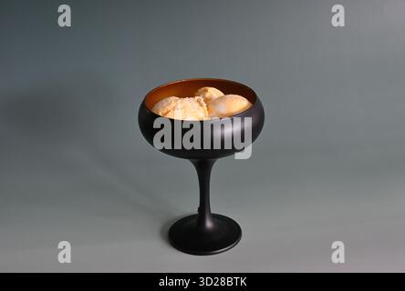 Schwarze Schüssel mit drei Kugeln Eis auf grauem Hintergrund Stockfoto