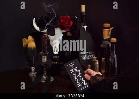 Hand hält eine schwarze Karte mit Hexenrunen in einem witzig-ästhetischen Stillleben Stockfoto