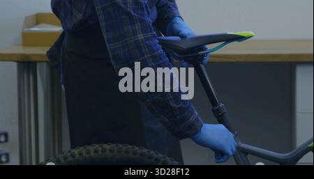 Einstellen der Mechaniker mit Handschuhen Positionieren der Sattelhöhe in der Werkstatt mit dem Rahmen des Mountainbikes Stockfoto