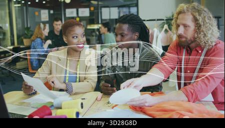Zusammenarbeit von Modedesignern in Blazern, die Papiermuster im Studio mit orangefarbenem Stoff anpassen Stockfoto