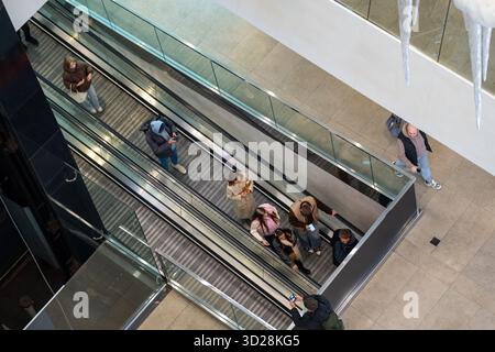 Hochwinkelaufnahme von Personen auf Rolltreppen in einem modernen Einkaufszentrum. Die Szene fängt mit conte den dynamischen urbanen Lebensstil und die Aktivität der Verbraucher ein Stockfoto