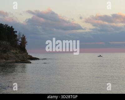Ruhiger rosa Sonnenuntergang über der Ägäis bei Fanari, Thrakien. Griechenland, mit einem kleinen Boot, das auf stillen Wasser driftet und weiche Wolken, die den Abend reflektieren. Stockfoto