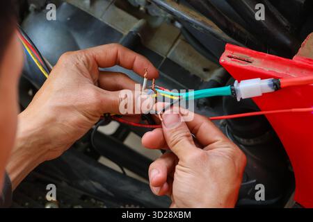 Nahaufnahme von bunten Drähten in den Händen eines Automechanikers, der Drähte zur Reparatur der elektrischen Anlage eines Motorrads verbindet. Stockfoto