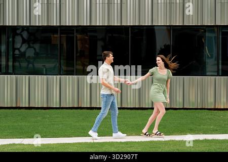 Ein junges Paar, das Hand in Hand vor einem modernen Gebäude läuft Stockfoto