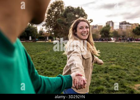 Frau, die Hand hält, führt einen Mann im Park Stockfoto