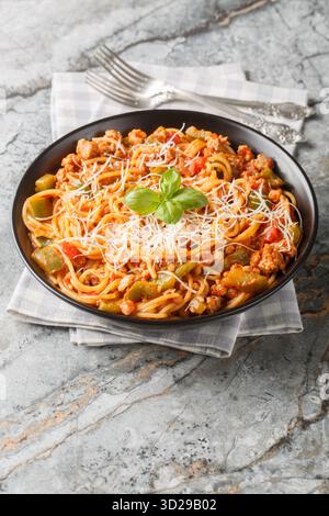 Spaghetti aus Chicago mit Wurst, Rindfleisch, grüner Paprika und feiner Tomatensauce auf dem Teller auf dem Tisch. Vertikal Stockfoto