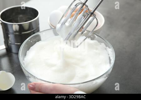 Frau, die Eiweiß mit Mixer am grauen Tisch schlägt, Nahaufnahme Stockfoto
