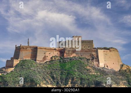 Eine beeindruckende historische Burg auf einem Hügel, mit Steinmauern, befestigten Strukturen und einem malerischen grünen Hügel mit einem hellblauen Himmel. Stockfoto