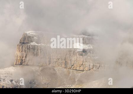 Hoch aufragende Klippen mit Blick auf einen dichten Wald und schneebedeckte Gipfel schaffen einen atemberaubenden Kontrast aus Texturen und Farben. Stockfoto
