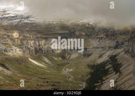 Hoch aufragende Klippen mit Blick auf einen dichten Wald und schneebedeckte Gipfel schaffen einen atemberaubenden Kontrast aus Texturen und Farben. Stockfoto