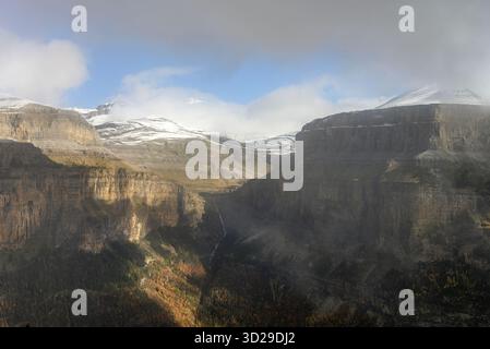 Hoch aufragende Klippen mit Blick auf einen dichten Wald und schneebedeckte Gipfel schaffen einen atemberaubenden Kontrast aus Texturen und Farben. Stockfoto