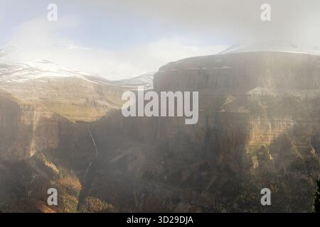 Hoch aufragende Klippen mit Blick auf einen dichten Wald und schneebedeckte Gipfel schaffen einen atemberaubenden Kontrast aus Texturen und Farben. Stockfoto