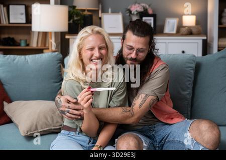 Glückliches Paar, das zu Hause einen positiven Schwangerschaftstest feiert, fröhliche Ankündigung, emotionales Lächeln und die ersten Momente, in denen man gemeinsam Eltern wird. Stockfoto