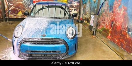Berlin, Deutschland - 18. Mai 2025: Blue Mini Cooper wird in einer Waschanlage mit lebendigem Hintergrund gewaschen. Stockfoto