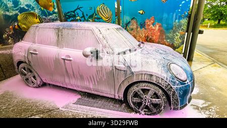 Berlin, Deutschland - 18. Mai 2025: MINI Cooper ist in einer Autowaschanlage mit Schaum bedeckt und hat eine lebhafte Unterwasserszene dahinter. Stockfoto