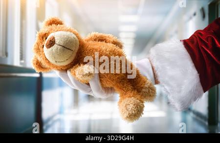 Konzept des Weihnachtsspiels an hospitalisierte Kinder zu Weihnachten mit der Hand des Weihnachtsmanns, die einen weißen Handschuh trägt und einen Teddybären in einem Krankenhausflur hält Stockfoto