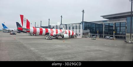 Berlin, 25. April 2025: Ein Flugzeug mit rot-weißen Streifen parkt an einem modernen Flughafenterminal. Stockfoto