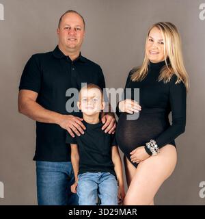 Das Porträt der Studio-Familie von erwartenden Eltern mit ihrem Sohn, schwarz gekleidet, symbolisiert Einheit und Eleganz Stockfoto