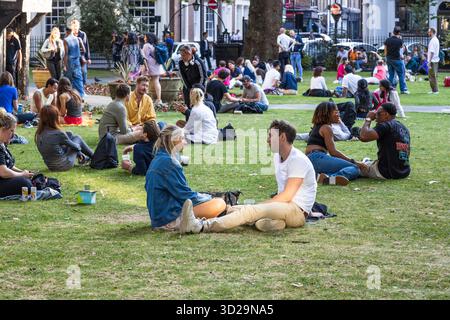 Junge Erwachsene hängen in einem belebten Stadtpark ab und picknicken auf dem Gras. London, UK, 23. Juli 2023 Stockfoto