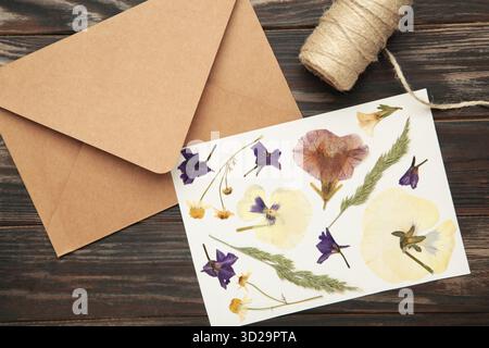 Gepresste und getrocknete Blüten mit Garn auf braunem hölzernem Hintergrund. Stockfoto