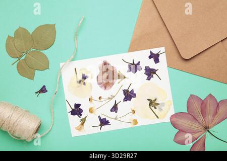 Gepresste und getrocknete Blüten mit Garn auf minzfarbenem Hintergrund. Stockfoto