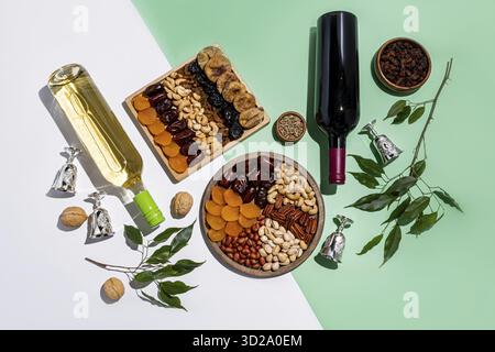 Zwei Holztabletts mit einer Mischung aus getrockneten Früchten und Nüssen, zwei Flaschen Rot- und Weißwein, Gläser Wein, grüne Äste. Soll shvat sein. Draufsicht Stockfoto