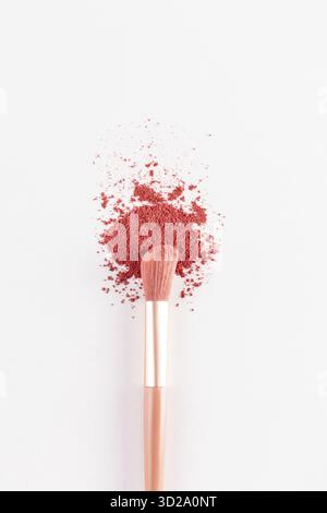 Ein schöner Schminkpinsel liegt auf einer Probe von trockenem, verstreutem Rouge in einem rosa Ton auf weißem Hintergrund. Die vertikale Ansicht von oben. Dekorative Kosmetik Stockfoto