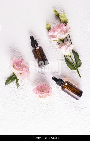 Draufsicht auf Kosmetikflaschen aus dunklem Glas mit einer Pipette mit einem natürlichen Gesichtspflegeprodukt. . Flache Lagen. Weißer strukturierter Hintergrund, Blumen Stockfoto