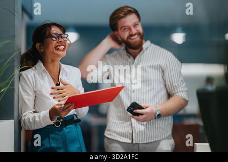 Zwei Kollegen lachen im Büro, während eine Frau ein rotes Klemmbrett hält Stockfoto
