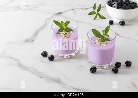 Zwei Glasgläser mit frisch zubereiteten Bio-Smoothies auf weißem Marmorhintergrund mit Brombeeren. Natürliche Entgiftung. Obstdessert Stockfoto