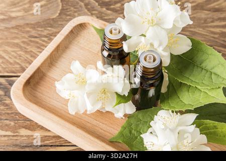 Natürliches ätherisches Jasminöl in zwei medizinischen Glasflaschen mit einem Tropfer auf einem Holztablett zwischen den Blüten des Jasmins. Das Konzept eines Spa Stockfoto