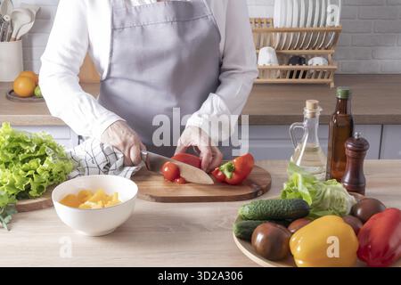 Eine ältere Frau schneidet rote Paprika auf einem Schneidebrett. Nahaufnahme der Küche und Arbeitsflächen mit Gemüse in einer Schüssel Stockfoto
