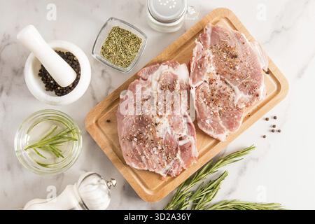 Zwei Stücke frisches rohes Schweinefleisch auf dem Küchenbrett und Marmortisch für gegrillte Steaks mit Gewürzen. Draufsicht Stockfoto