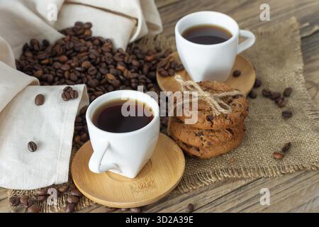 Zwei Tassen frisch gebrühter Espresso auf Holztisch. Kaffeebohnen und Crunchie Cookies auf hellem Holztisch, rustikaler Stil, hausgemacht Stockfoto