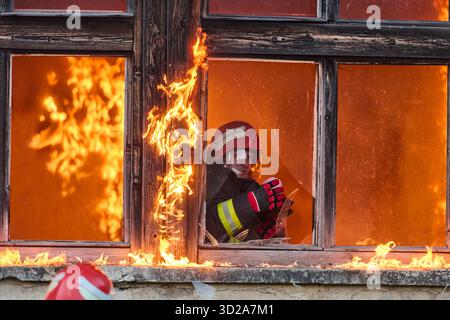 Ein Feuerwehrmann rettet ein Baby aus einem brennenden Gebäude. Der Feuerwehrmann ist in Aktion und rettet das Kind aus der Notsituation. Dieses Bild kann verwendet werden, um Themen von Tapferkeit, Rettungseinsätzen und Rettungsdiensten zu veranschaulichen. || Modell freigegeben Stockfoto