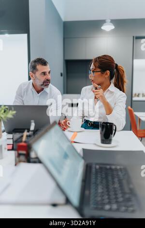 Multikulturelles Geschäftsgespräch zwischen Kollegen in einem modernen Büro mit Laptops und Kaffee Stockfoto