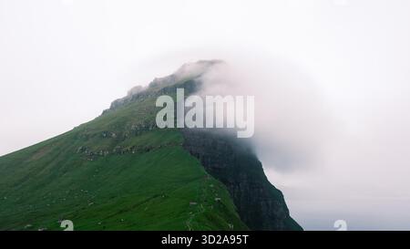 Dramatische Klippen der Färöer erheben sich majestätisch aus dem Atlantik, umgeben von weichem, wirbelndem Nebel. Üppig grüne Hügel gegen den Nebel. Kallur Lighthouse, Kalsoy Island Stockfoto