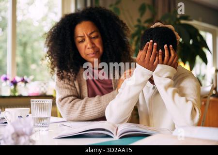Mutter tröstet Tochter, die frustriert wird, während sie zu Hause studiert Stockfoto