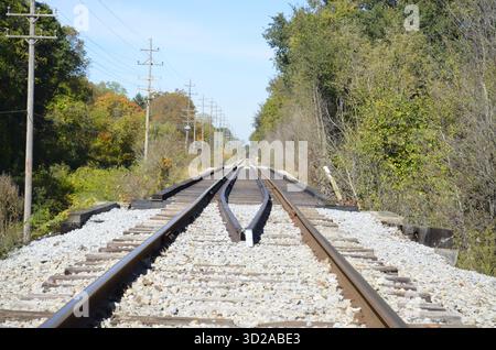 Verrostete Eisenbahnschienen mit zusätzlichen Schienen für Entgleisungsschutz und strukturelle Stabilität, wenn sie entlang einer Brücke über eine örtliche Straße oder Straße fahren. Stockfoto